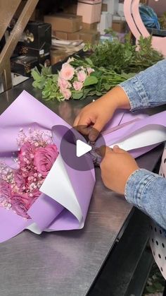 a woman is cutting paper with scissors and flowers on the table in front of her