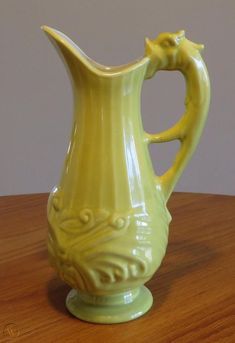 a yellow ceramic pitcher sitting on top of a wooden table next to a gray wall