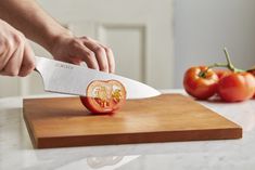 a person cutting up a tomato with a knife on a cutting board next to some tomatoes