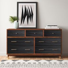 a black and brown dresser sitting on top of a wooden floor next to a plant