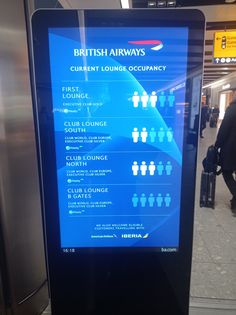 an airport information board showing the current arrival and departure times for british airways, with people walking by