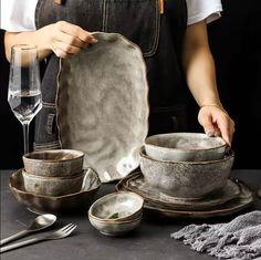 a woman is setting up dishes on a table with utensils and wine glasses