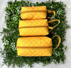 three yellow quilted bags sitting on top of green plants