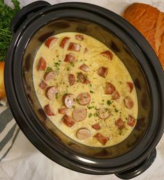 a crock pot with ham and cheese in it on a table next to bread