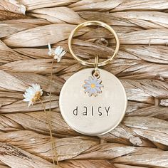 a keychain with the word daisy written on it next to some daisies