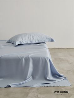 an unmade bed with blue sheets and pillows on it's side, in front of a white wall