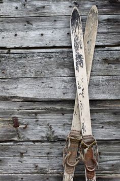 two pairs of skis are propped up against a weathered wood planked wall with snow shoes on it