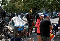 people are standing on the sidewalk near bikes and other items in baskets, bags, and umbrellas