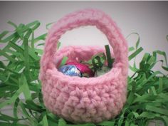 a pink crocheted basket with an easter egg in it on some green grass