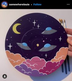 someone is holding up a paper plate with space and stars painted on it, along with paintbrushes