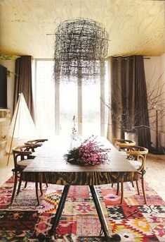 a dining room table with flowers on it in front of a large window and a chandelier hanging from the ceiling