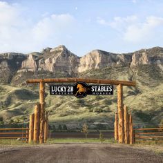 the entrance to lucky 2 stables in front of mountains and a dirt road with a horse on it