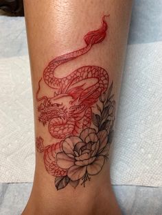 a tattoo on the leg of a woman with a dragon and flowers around her ankles