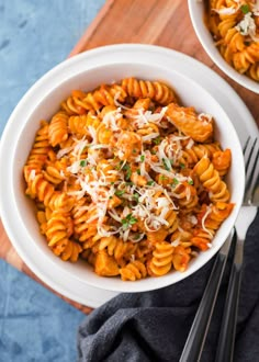 two bowls filled with pasta and parmesan cheese on top of a wooden cutting board