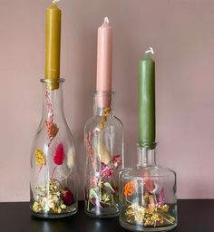 three glass vases with flowers and candles in them