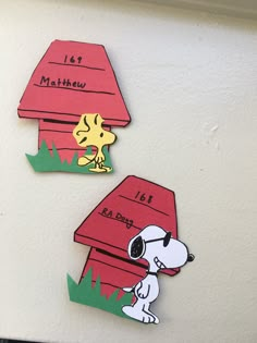 two magnets depicting snoopy and his doghouse are on the wall in front of each other