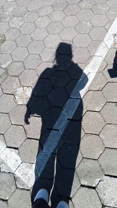 the shadow of a person standing in front of a parking meter with their shadows on the ground