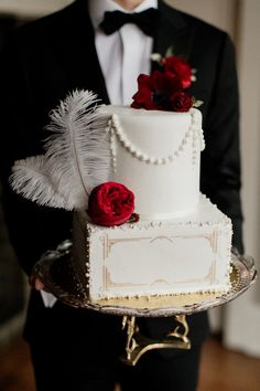 a man in a tuxedo holding a white and red wedding cake with feathers on it