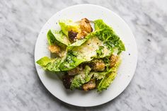 a white plate topped with lettuce covered in cheese and sauce on top of a marble table