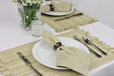 a table set with place settings and flowers in a vase on the table cloths