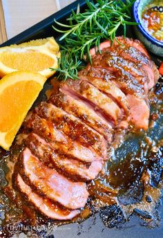 some meat and oranges on a black tray with seasoning sprinkled around it