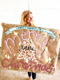 a woman holding up a merry christmas sign with a tree on it's side