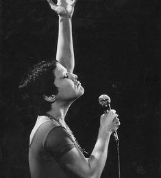 a black and white photo of a woman holding a microphone in the air with her right hand up