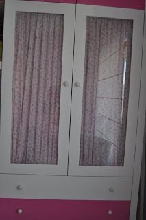 a white and pink armoire with two doors on each side, in front of a window