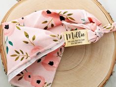 a pink flowered napkin with a name tag on it sitting on top of a wooden plate