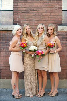 a group of women standing next to each other in front of a brick wall holding bouquets