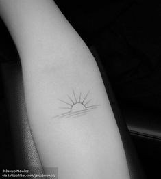 a black and white photo of a small sun tattoo on the left inner arm,