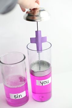 a person holding a purple cross in a beakle next to two glasses filled with pink liquid