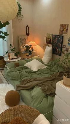 a bed with green sheets and pillows next to a plant in a room filled with pictures