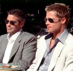 two men sitting next to each other in front of a table with food on it