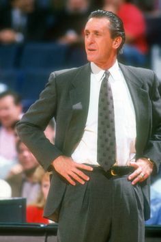 a man wearing a suit and tie standing in front of a basketball court with his hands on his hips