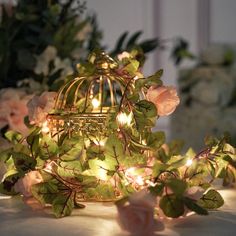 a birdcage filled with flowers and lights on top of a white table cloth