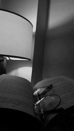 an open book sitting on top of a table next to a lamp with glasses on it