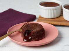 a piece of chocolate cake on a pink plate next to two small white bowls with brownies in them