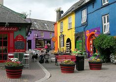 several colorful buildings with people sitting at tables in front of them and on the sidewalk