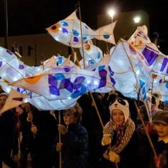 a group of people holding kites in the shape of fish with lights on them