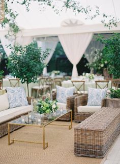 an outdoor seating area with wicker couches and coffee tables in front of a white tent