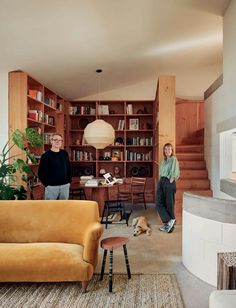 two people standing in a living room with bookshelves on the wall and a dog laying on the floor