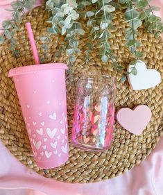 two cups with straws and hearts are sitting on a woven place mat next to a potted plant