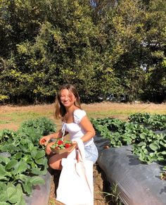 a woman kneeling down in the middle of a field with strawberries