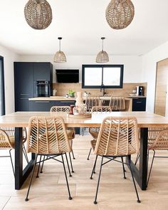 a dining room table and chairs in front of an open kitchen area with large windows