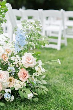 an arrangement of flowers and greenery on the ground at a wedding ceremony with white chairs in the background