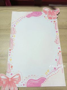 a pink and white paper with butterfly decorations on the edges, sitting on a wooden table