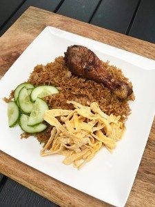 a white plate topped with rice and meat next to cucumbers on a wooden table