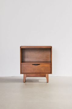 a small wooden cabinet sitting on top of a cement floor next to a white wall