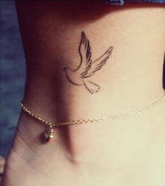 a small bird tattoo on the side of a woman's foot, with a chain around her ankle